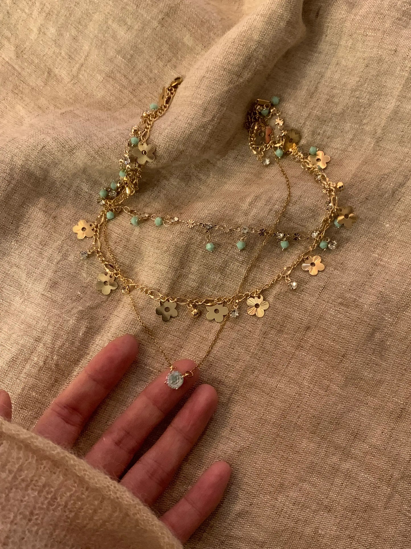 Gold flower necklace with turquoise beads and crystal accents, handcrafted minimalist jewelry on fabric