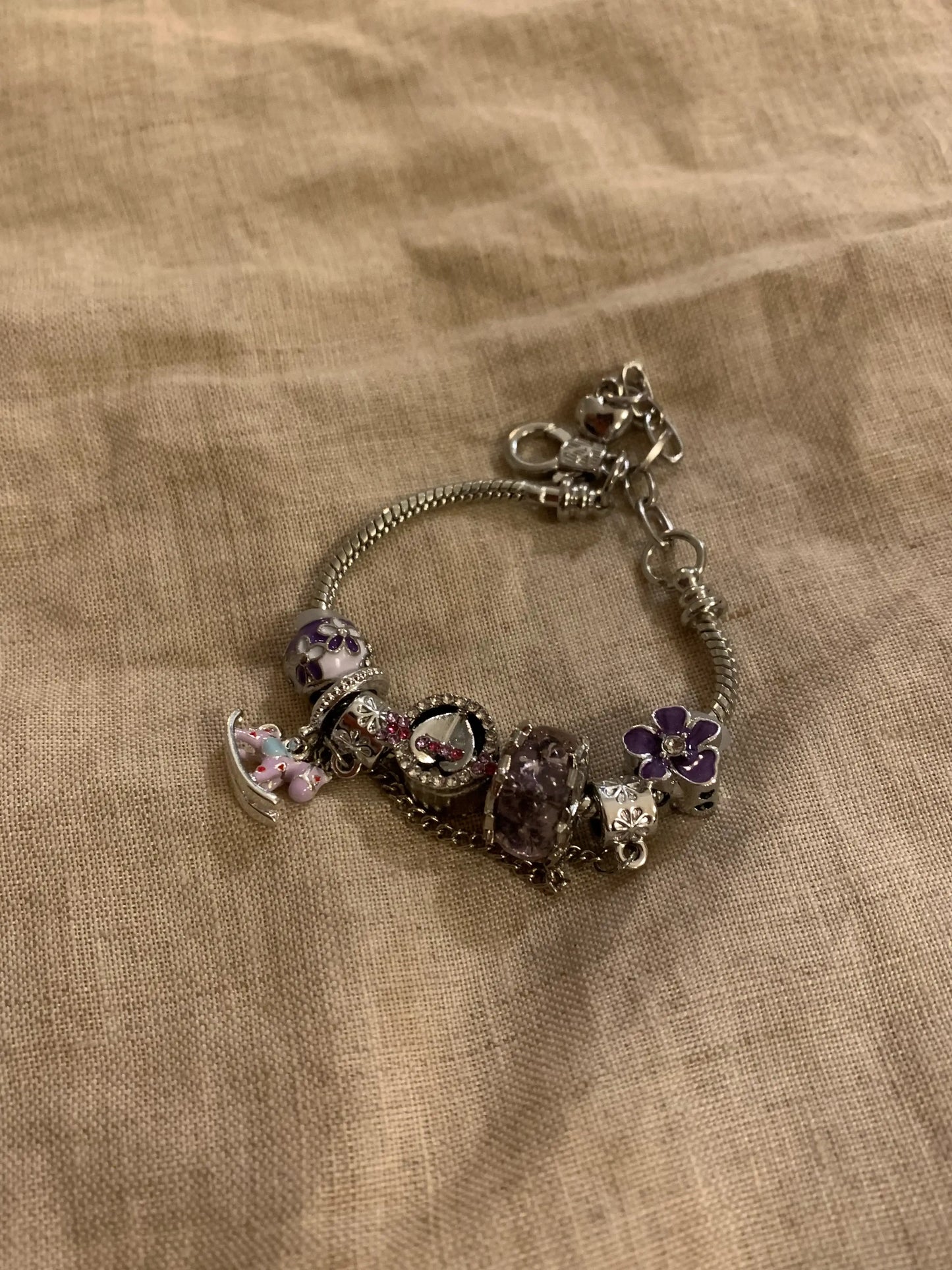 Silver charm bracelet with purple floral and gemstone beads on textured fabric