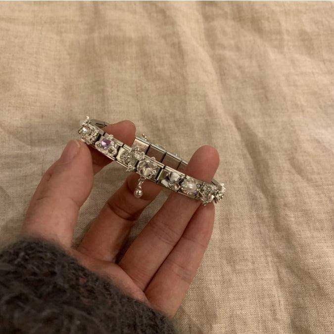 Elegant silver bracelet with sparkling gemstones and a dangling charm, held gently in hand.