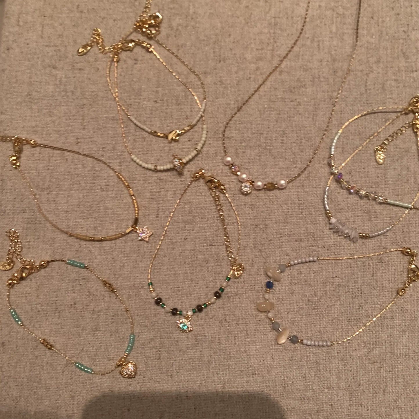 Elegant gold necklaces with beads, pearls, and charms on a textured backdrop