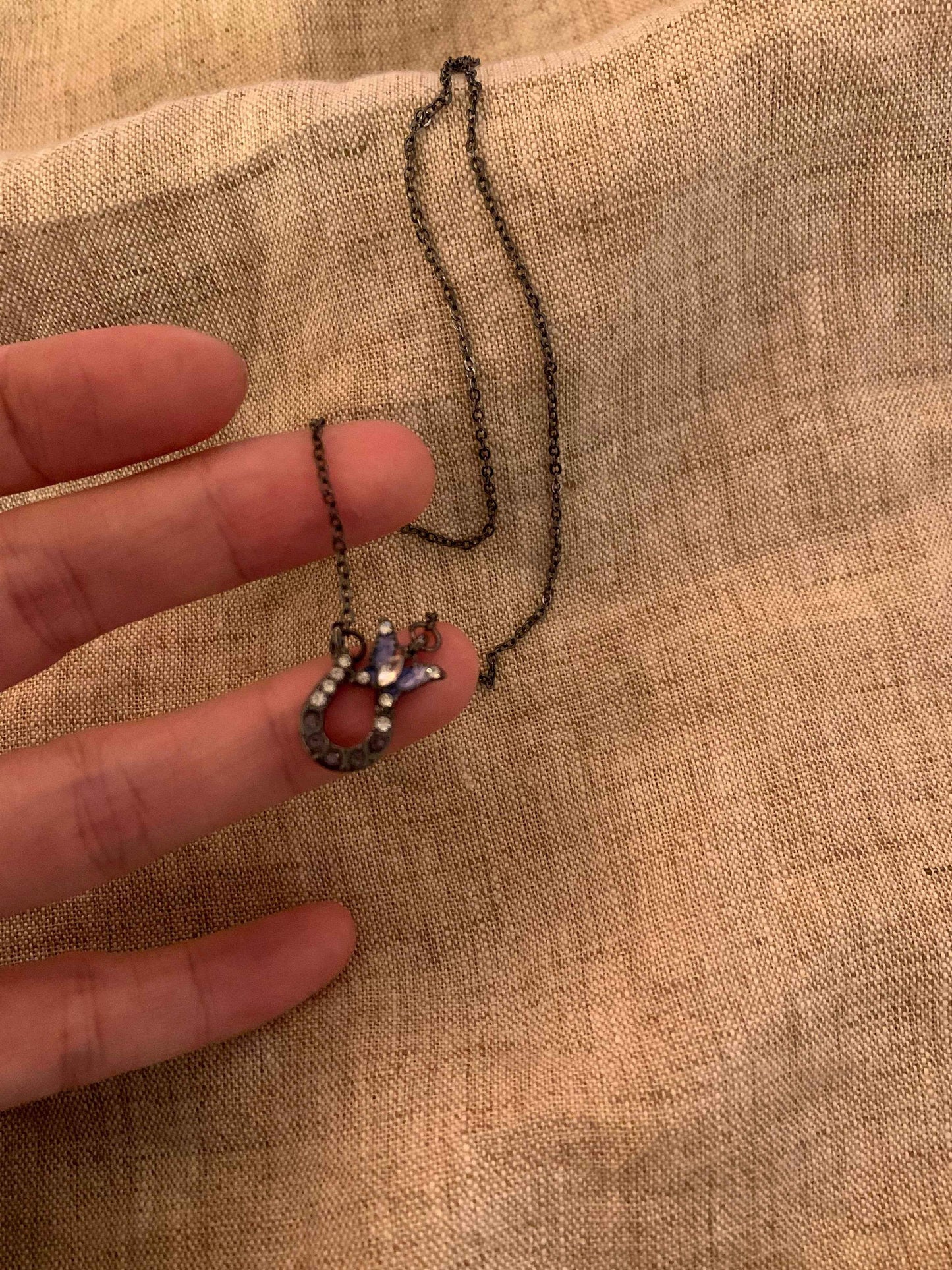 Minimalist necklace with blue gemstone pendant and delicate chain held against fabric background