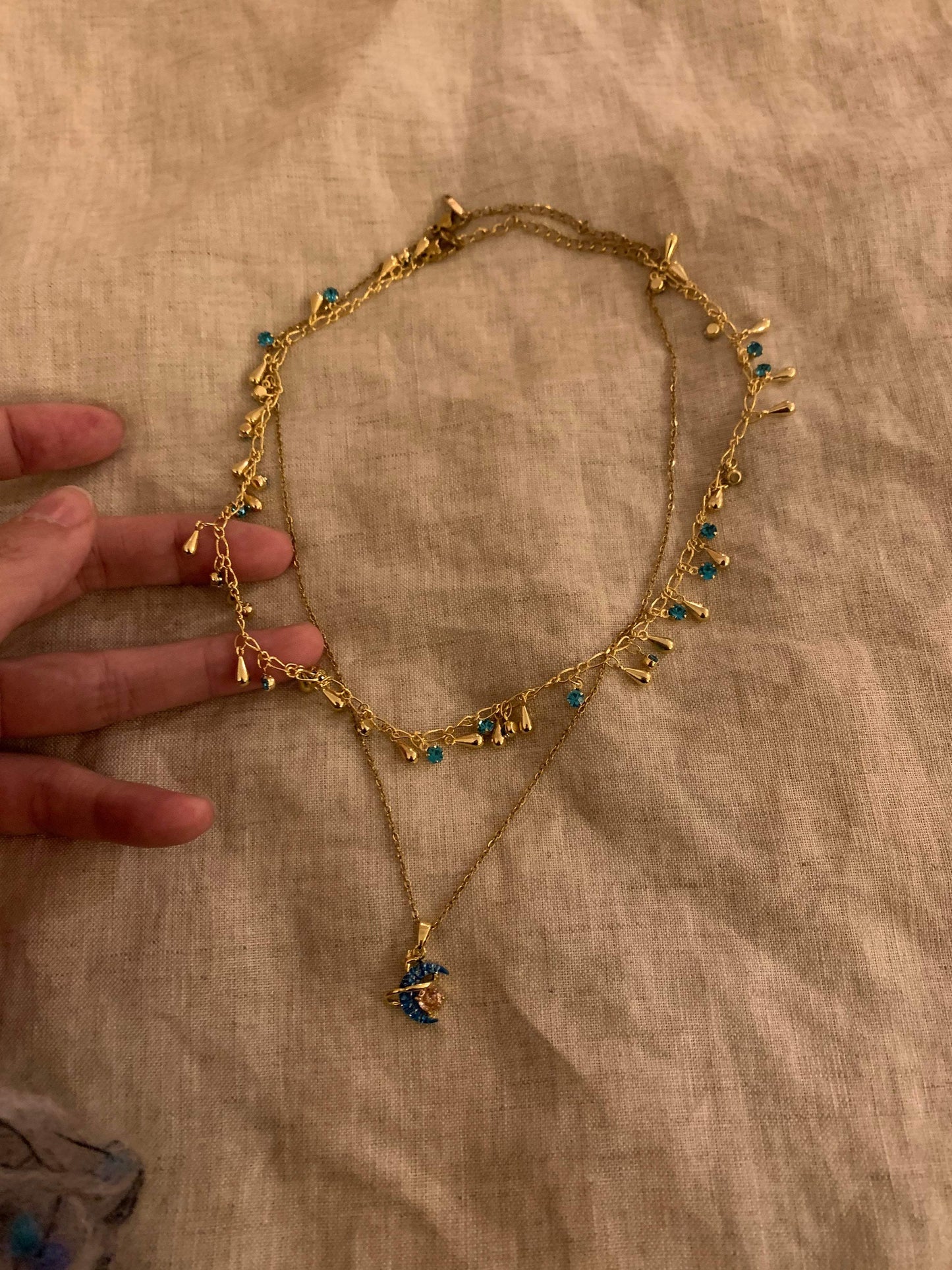 Gold necklace with blue gemstones and moon pendant, minimalist design on fabric background