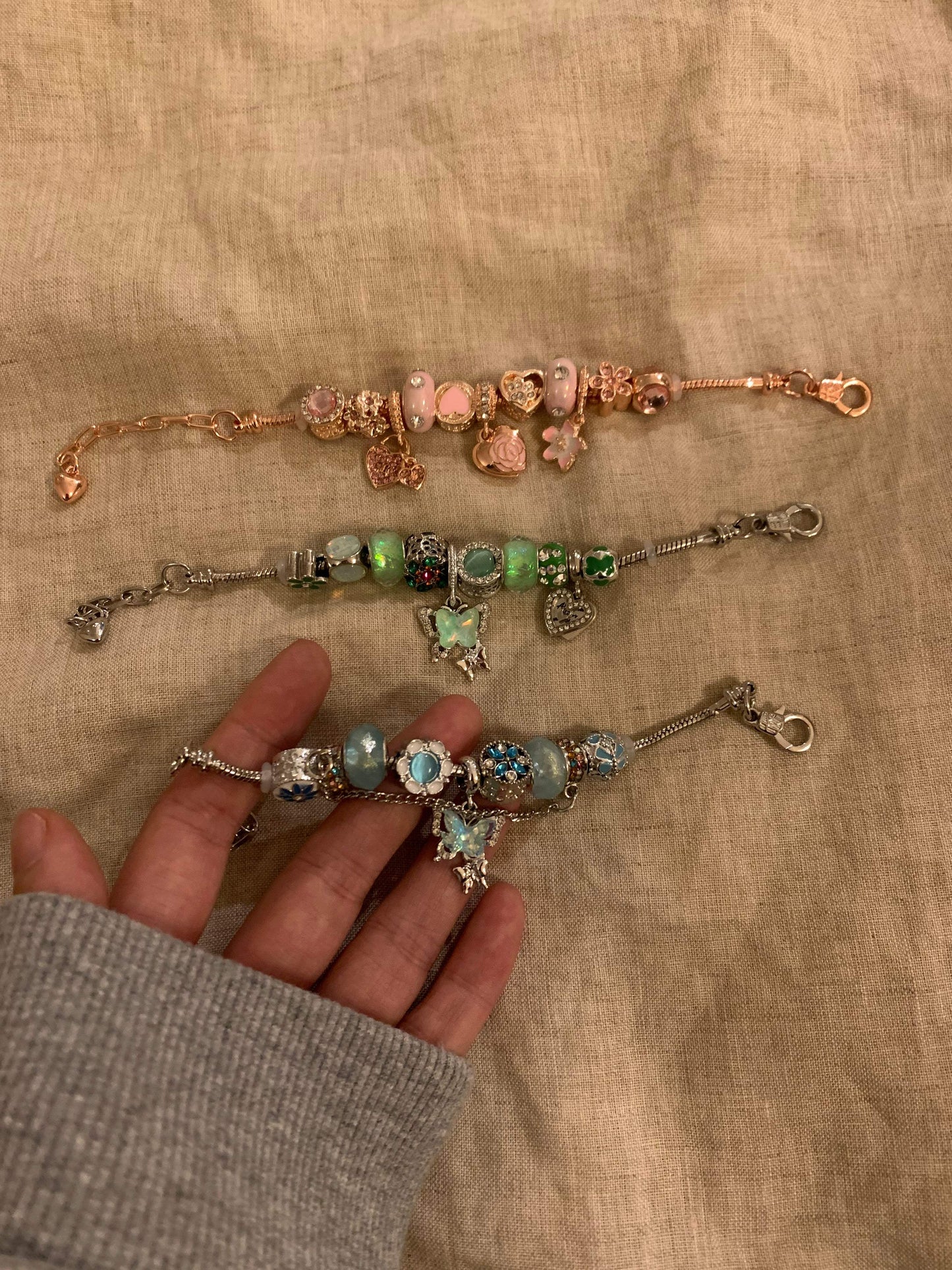 Three charm bracelets with colorful beads and butterfly charms, displayed on a hand against a fabric background.