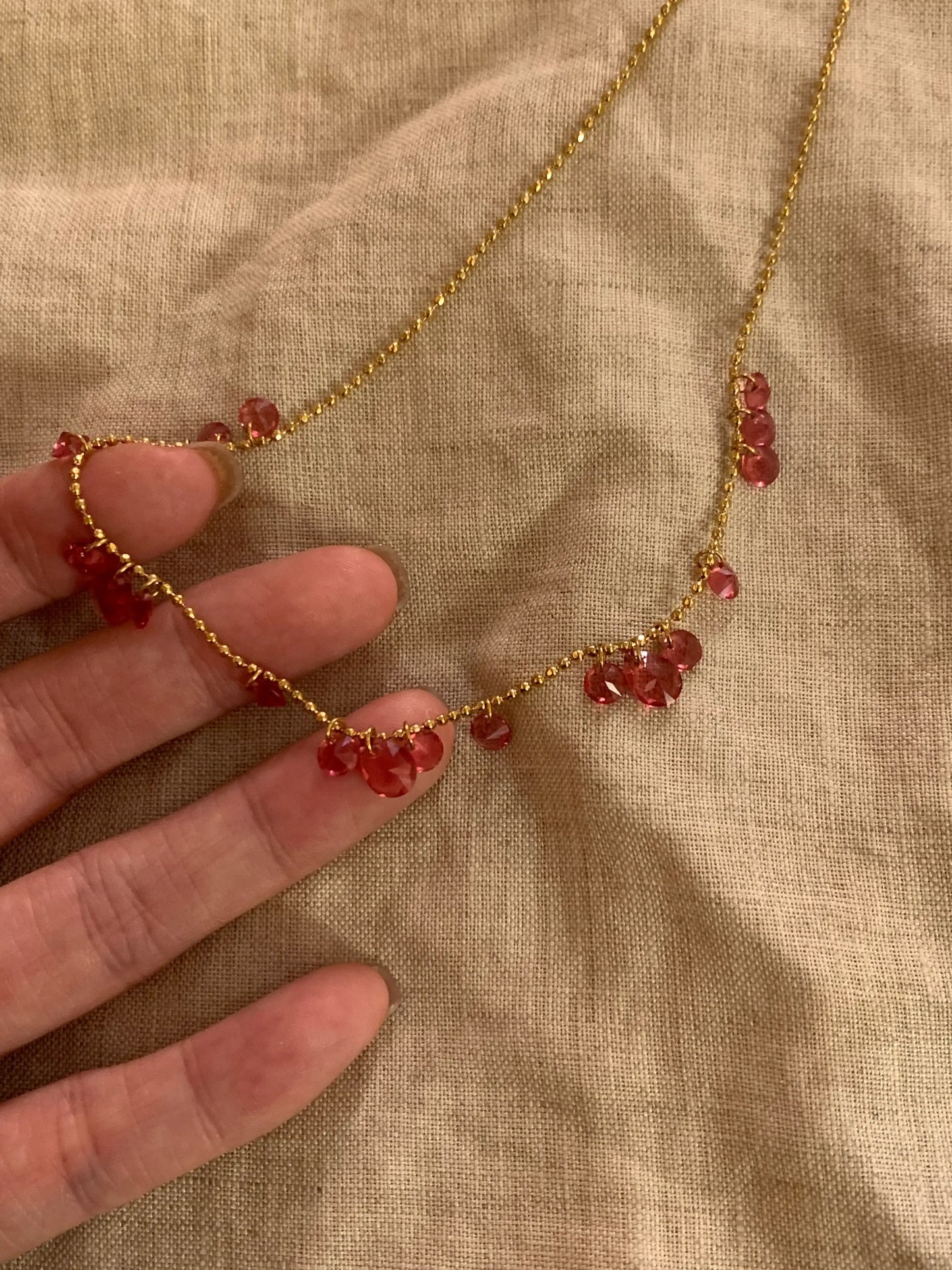 Gold chain necklace with red gemstone drops, hand holding delicate jewelry on fabric background