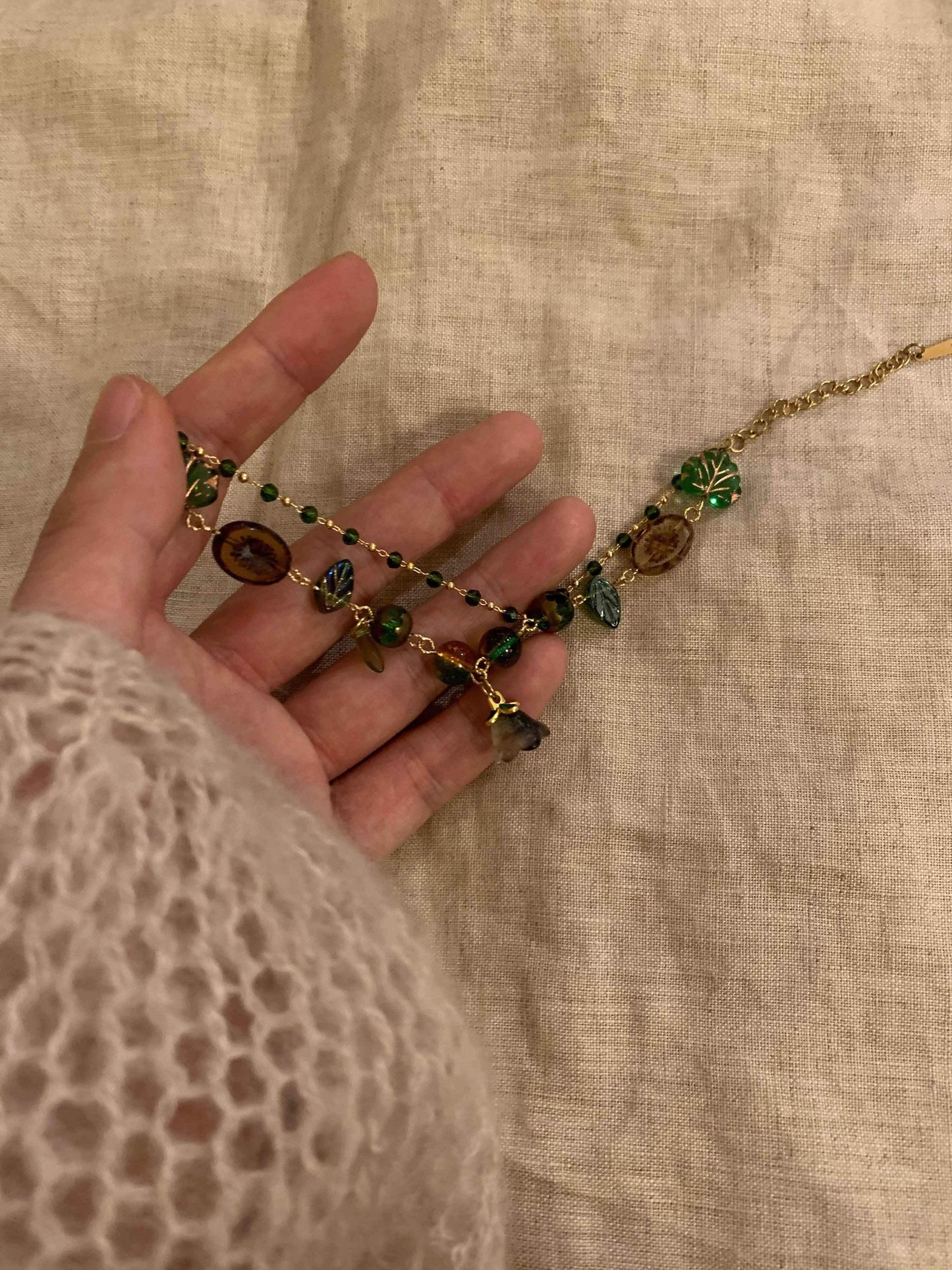 Hand holding delicate gold necklace with green leaf and amber beads, minimalist jewelry design