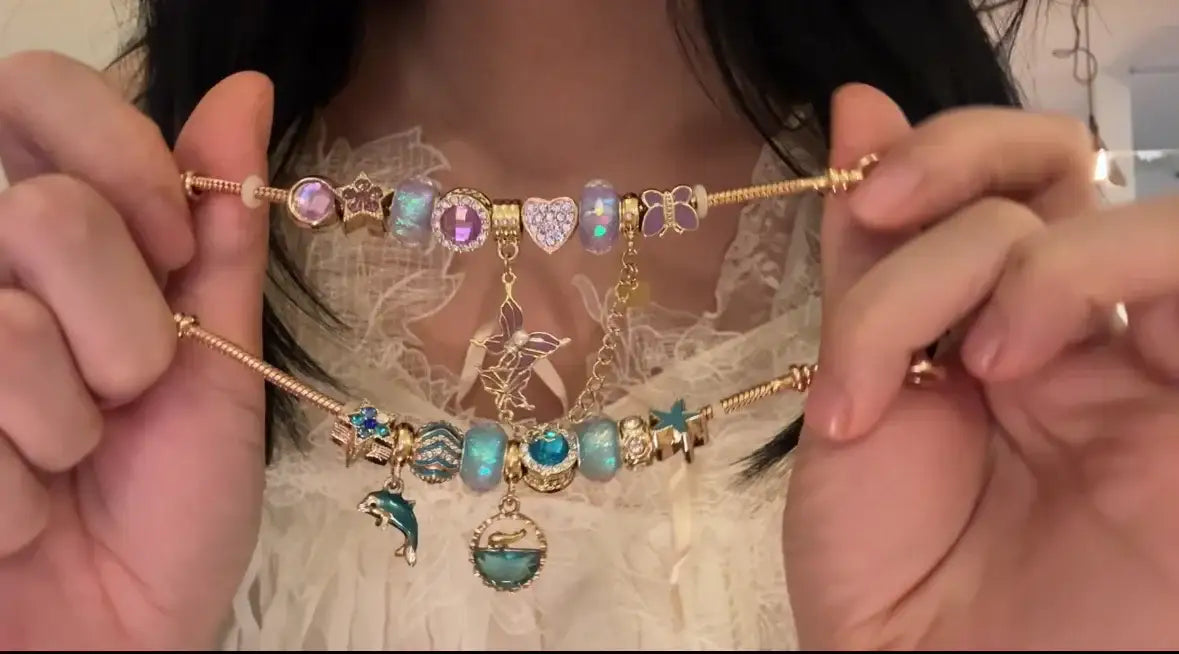 Gold charm bracelets with colorful beads, heart, butterfly, dolphin, and star charms, held by hands.