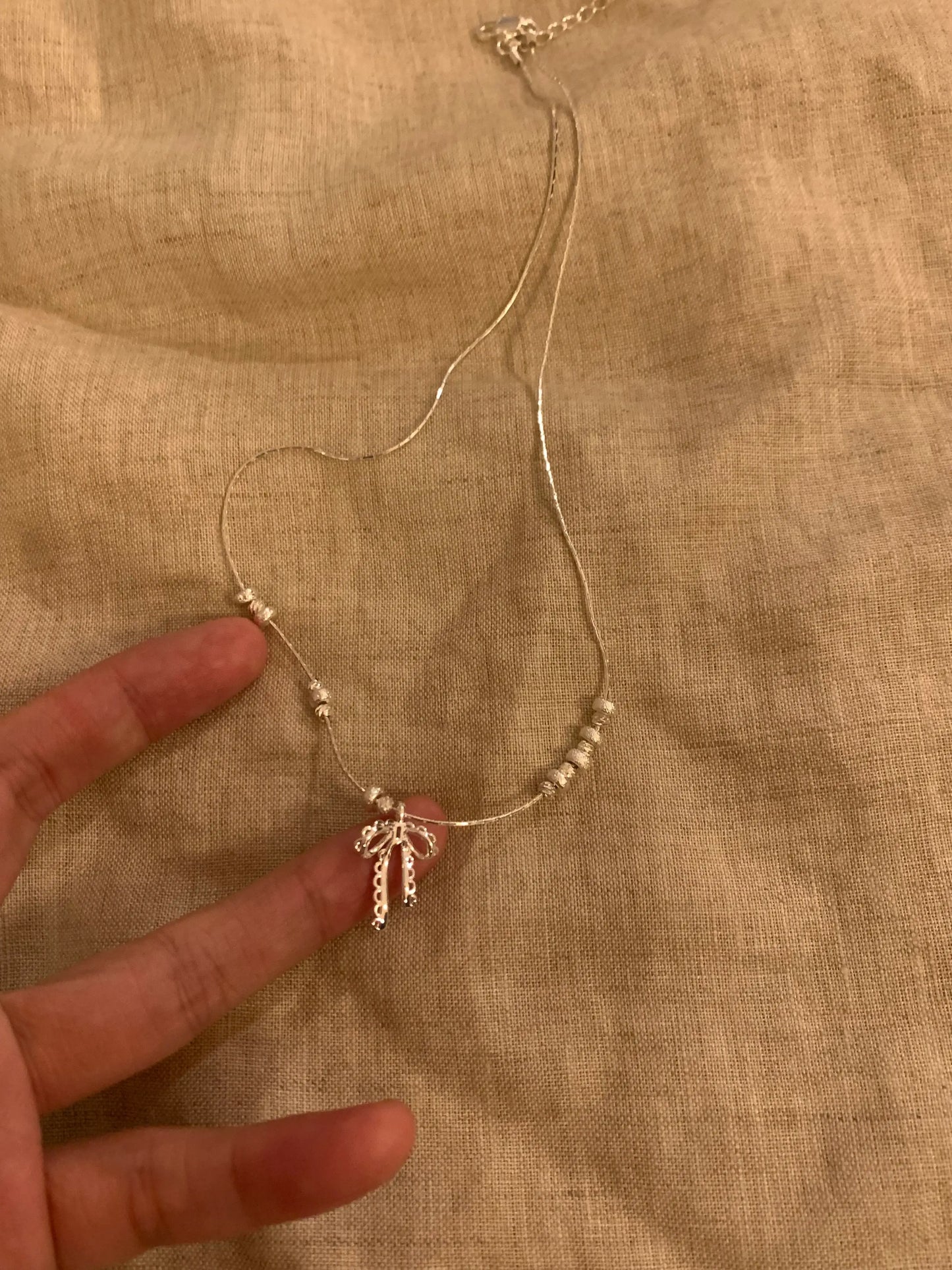 Delicate gold necklace with bow pendant and beaded chain, held against fabric background