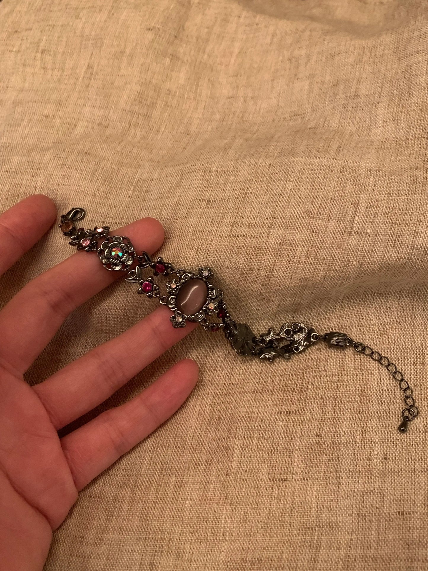 Vintage-style floral bracelet with pink rhinestones and oval stone, held on hand over linen