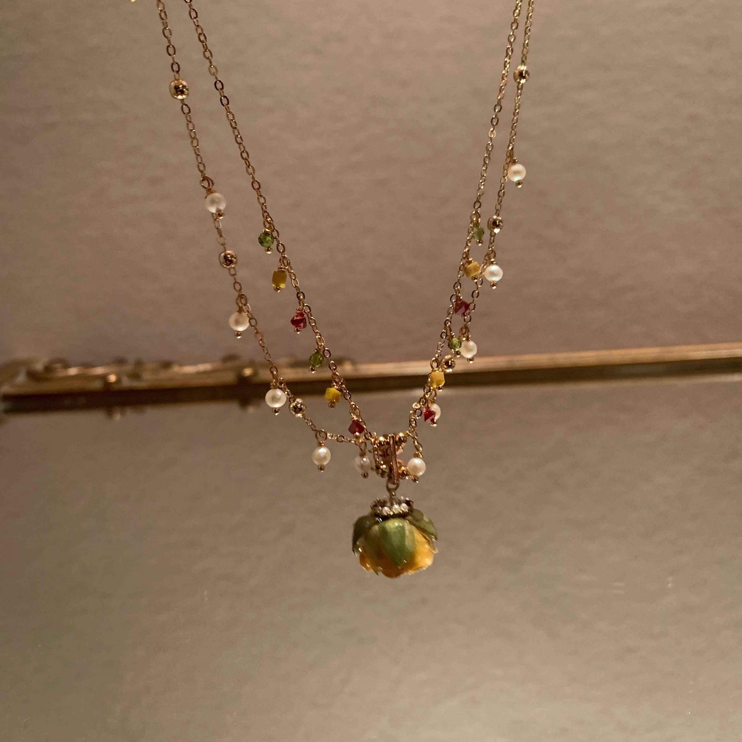 Gold chain necklace with colorful gemstones and a green flower pendant, minimalist jewelry design