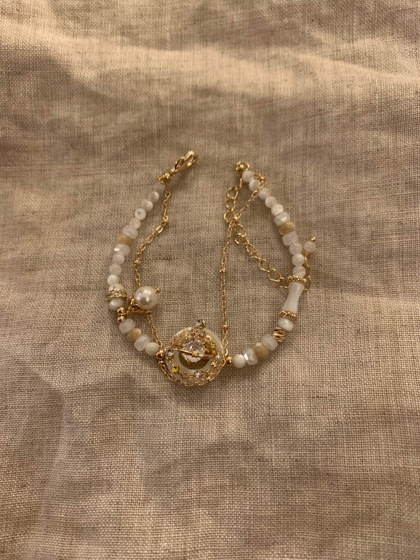 Elegant gold chain bracelet with white beads, pearl, and crystal centerpiece on linen background