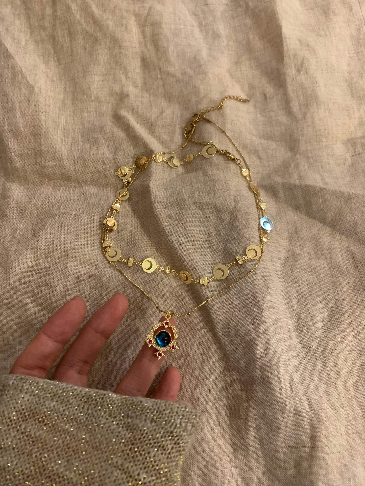 Gold moon charm necklace with blue gem pendant, handcrafted minimalist jewelry on linen background