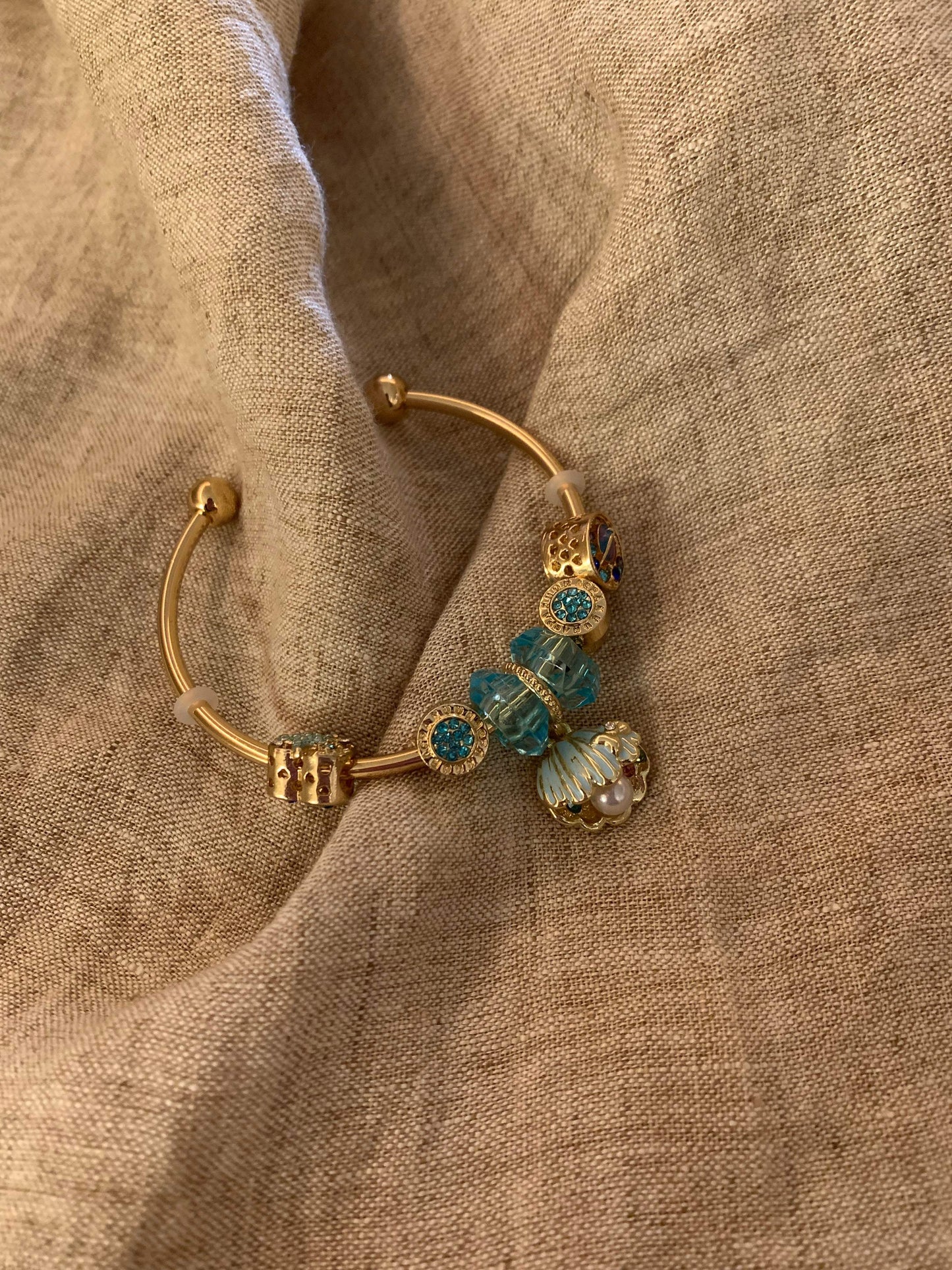 Gold charm bracelet with blue crystal beads and shell pendant on linen fabric