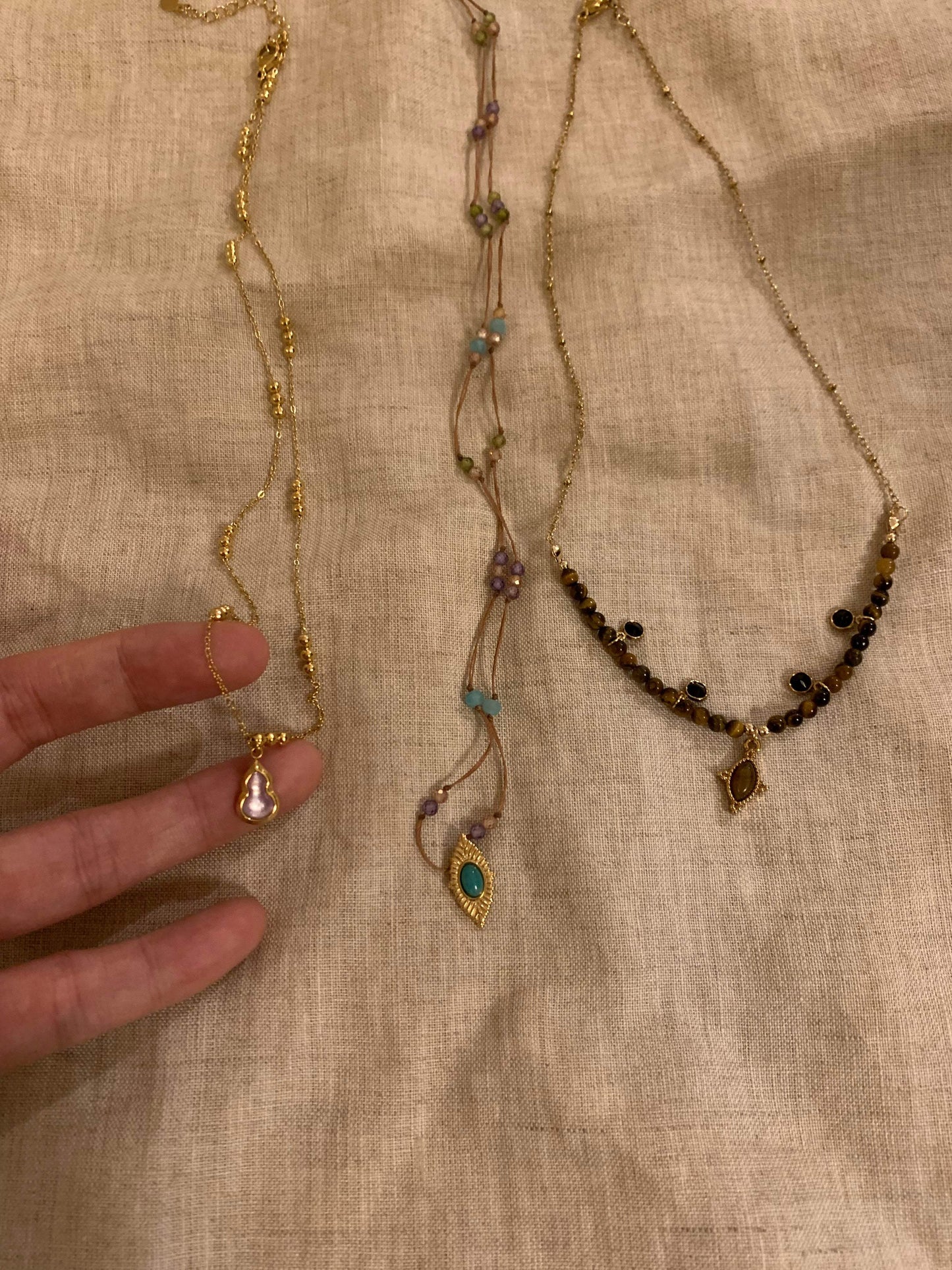 Elegant gold necklaces with gemstone pendants and beaded designs on a linen background