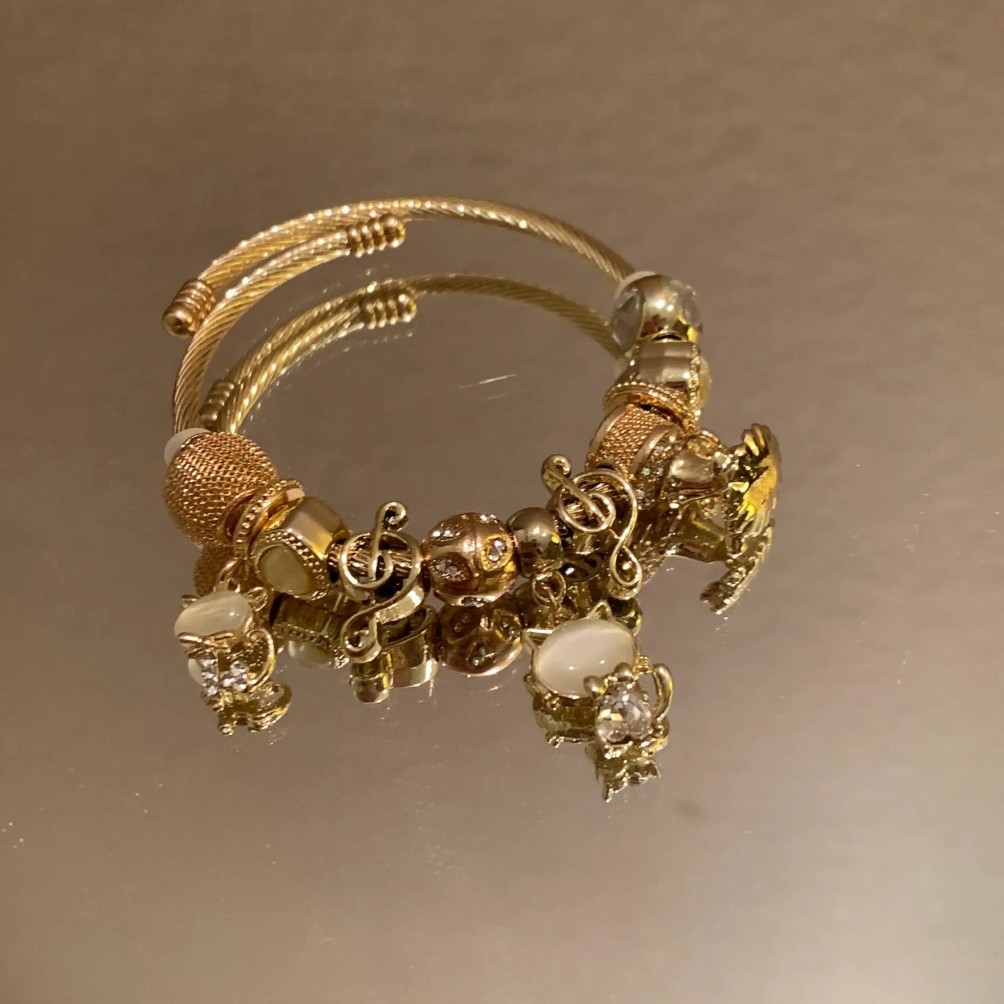 Gold charm bracelet with musical notes, crystals, and beads on a reflective surface