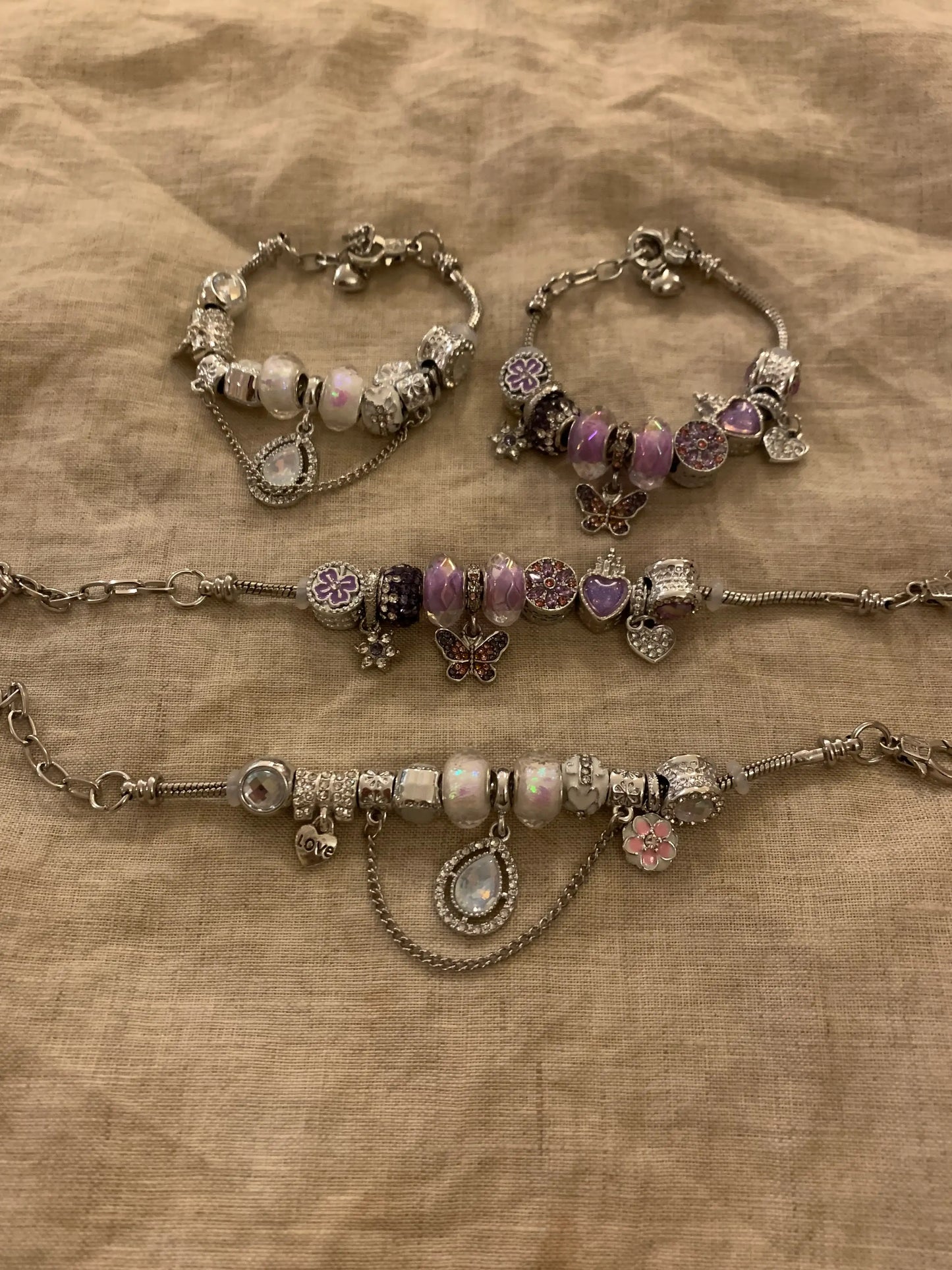Silver charm bracelets with purple, white beads, butterfly, flower, heart charms on fabric
