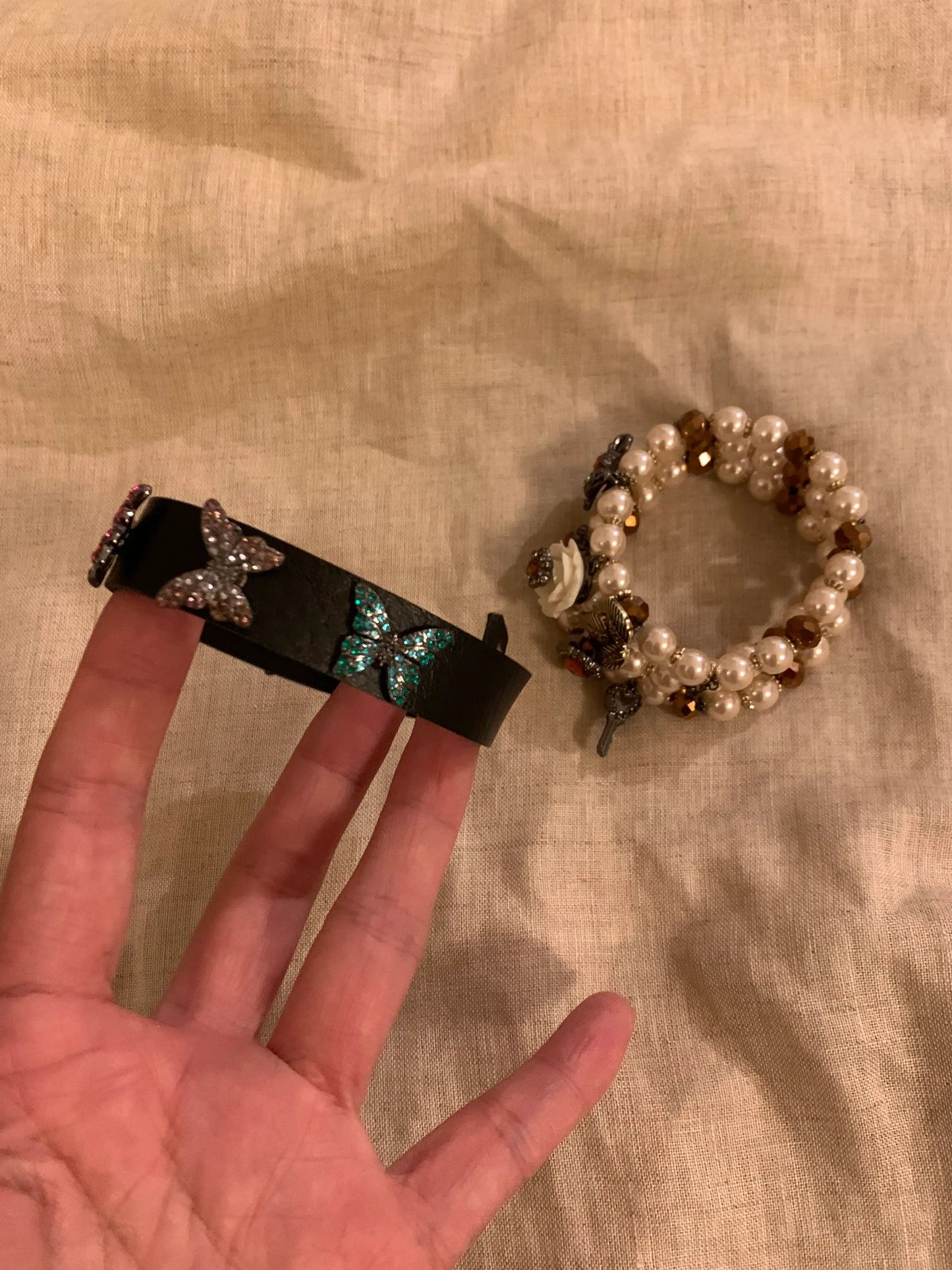 Black leather bracelet with butterfly charms and pearl beaded bracelet on fabric background