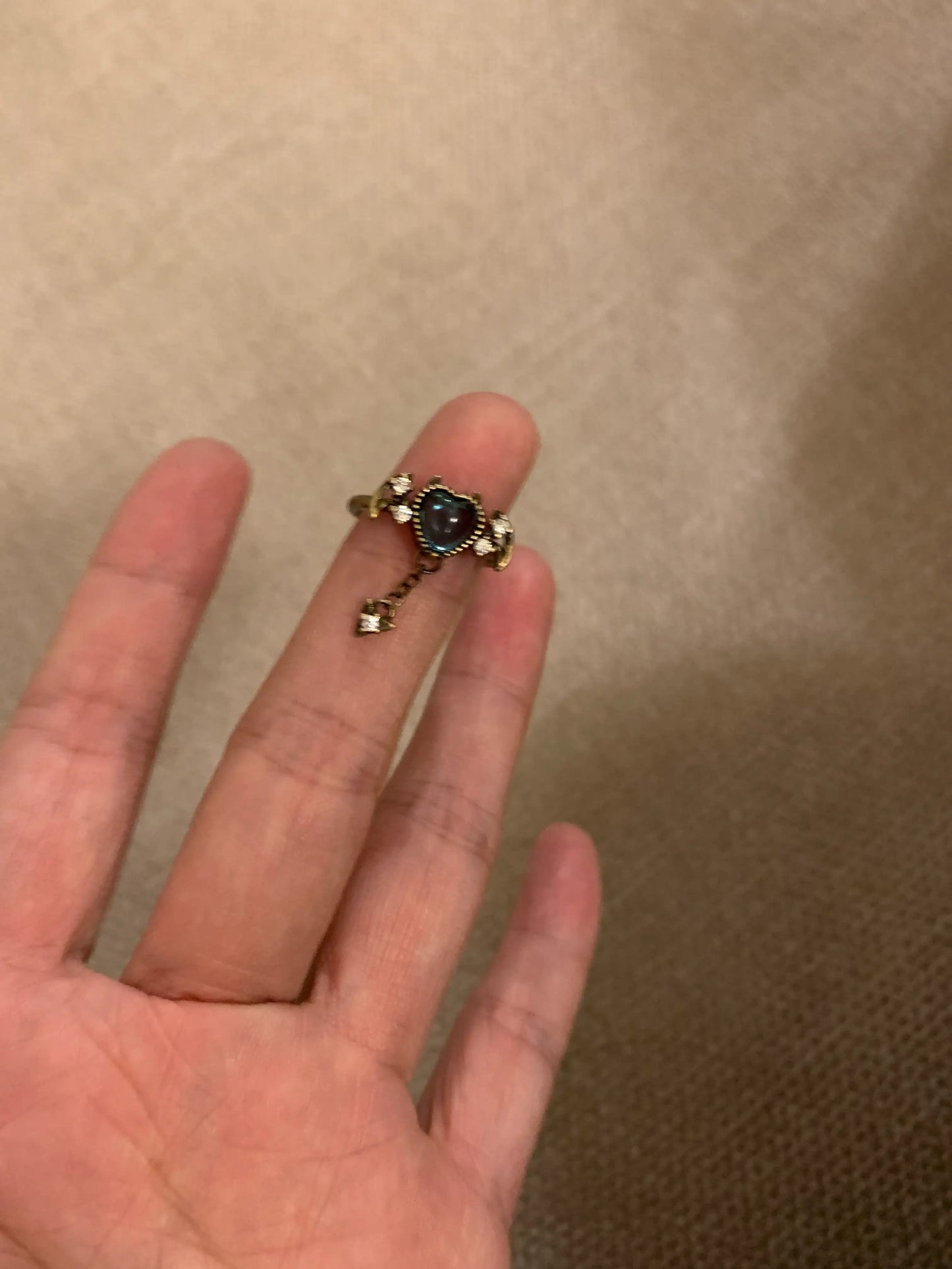 Gold ring with heart-shaped blue gemstone and dangling charm, held on finger