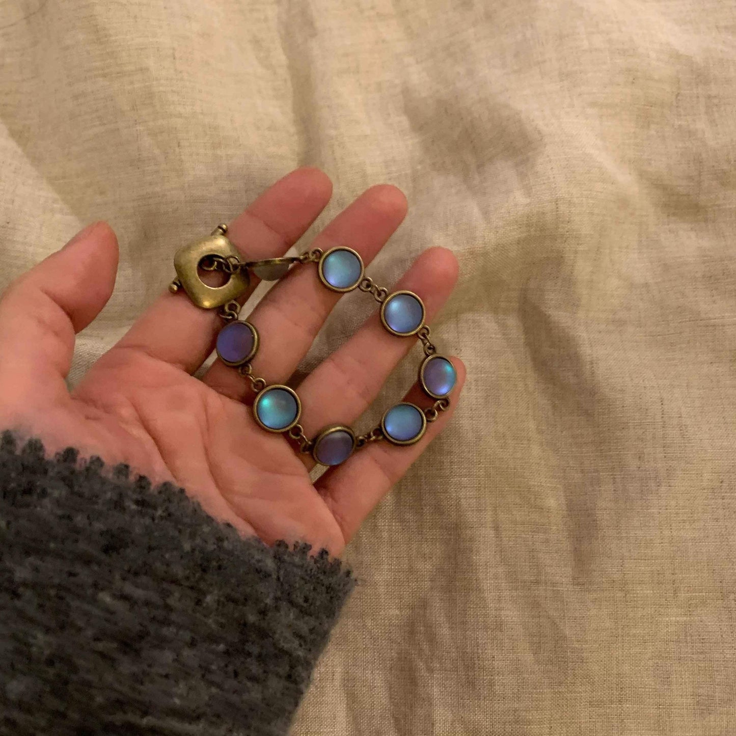 Hand holding vintage-style bracelet with iridescent blue stones and brass clasp, perfect for minimalist jewelry lovers