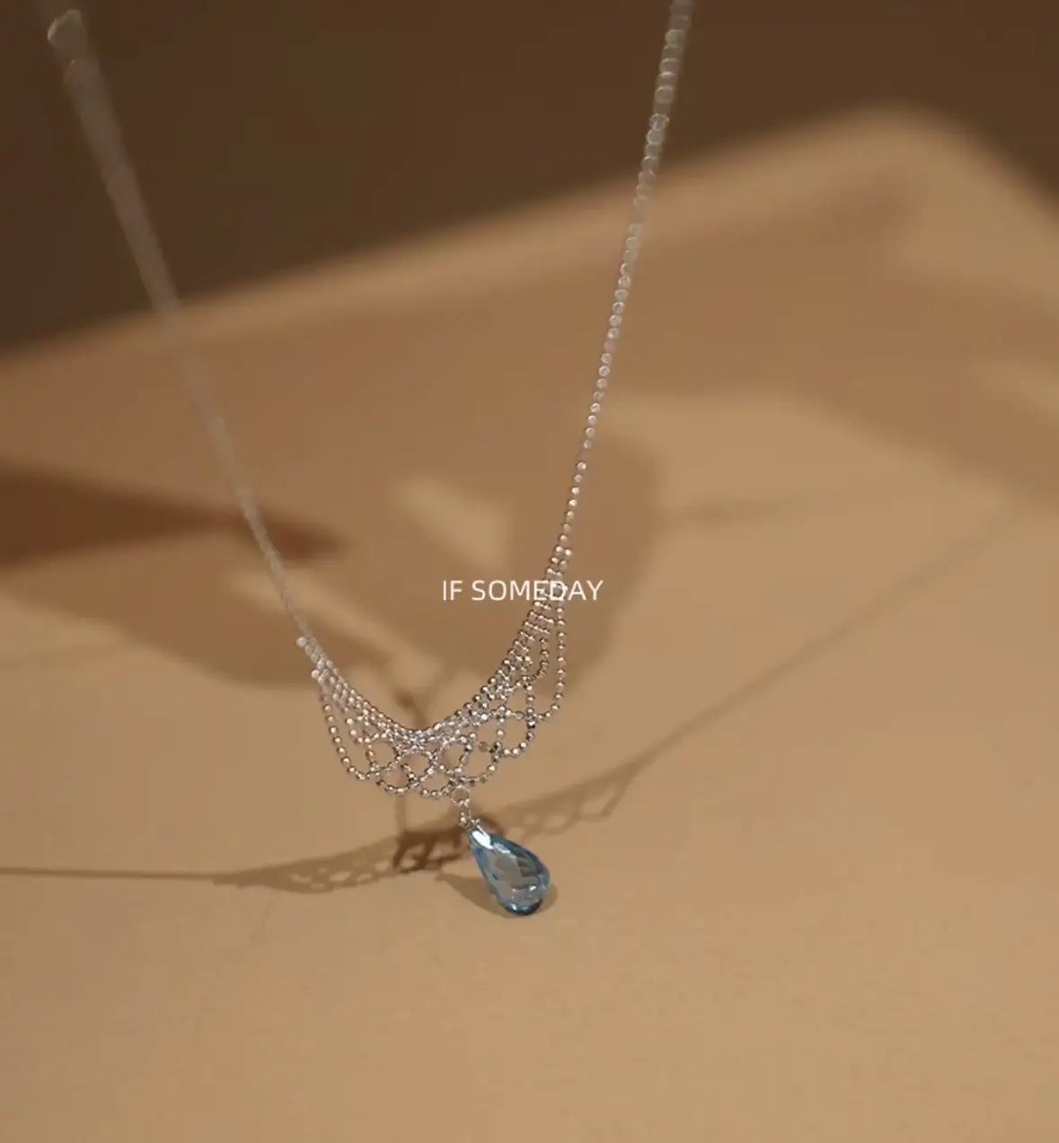Elegant silver necklace with blue teardrop pendant and intricate chain design