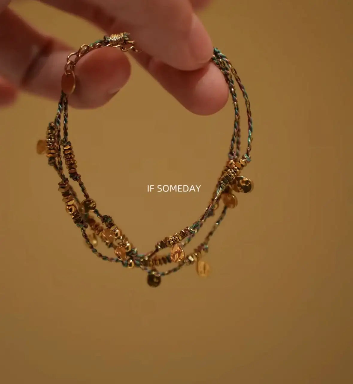 Layered gold charm bracelet with colorful threads and delicate beads, perfect for minimalist jewelry lovers