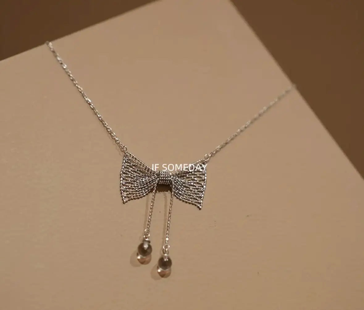 Delicate silver bow necklace with dangling beads, minimalist jewelry design