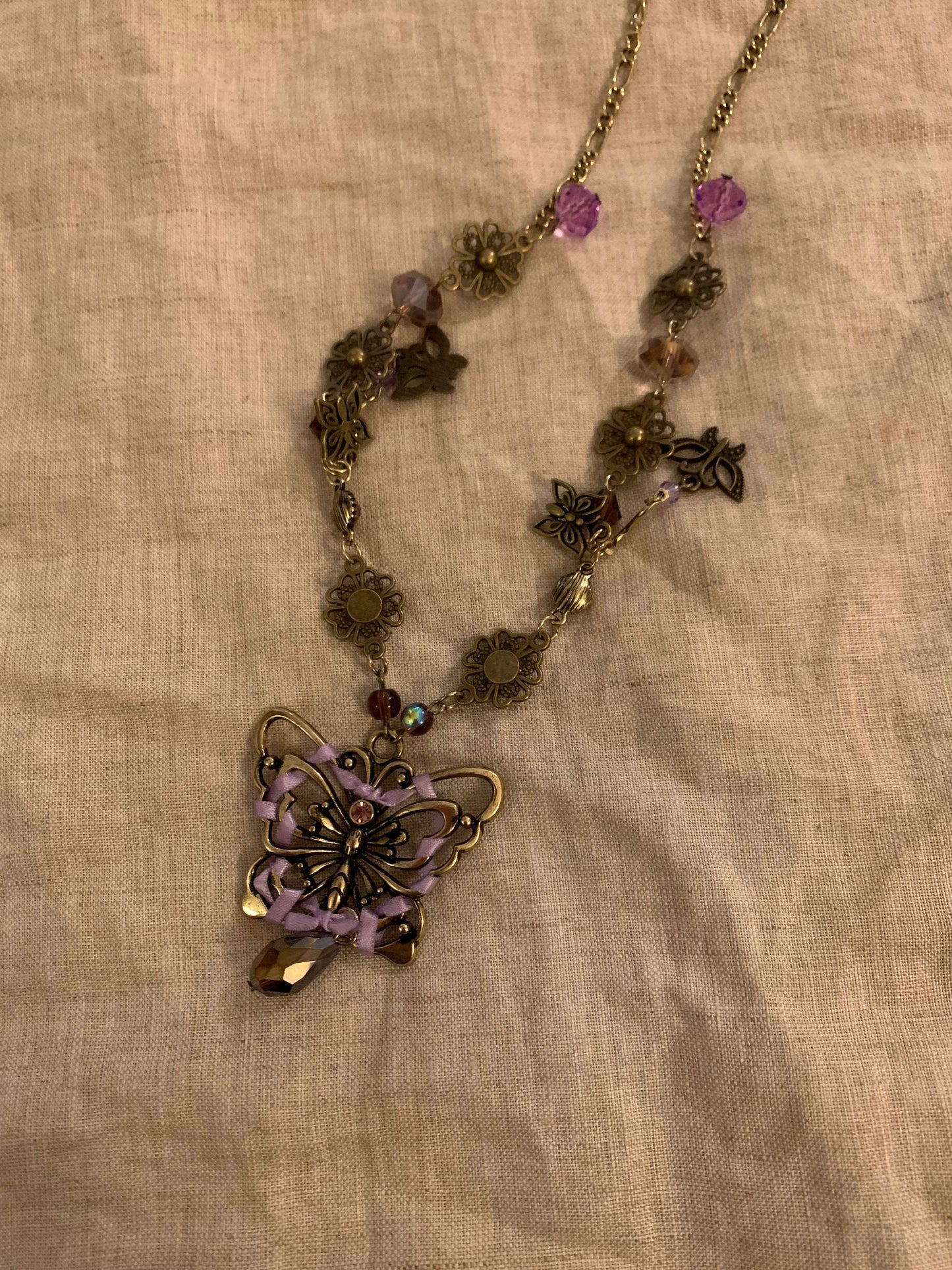 Boho butterfly necklace with purple ribbon, floral charms, and crystal beads on gold chain