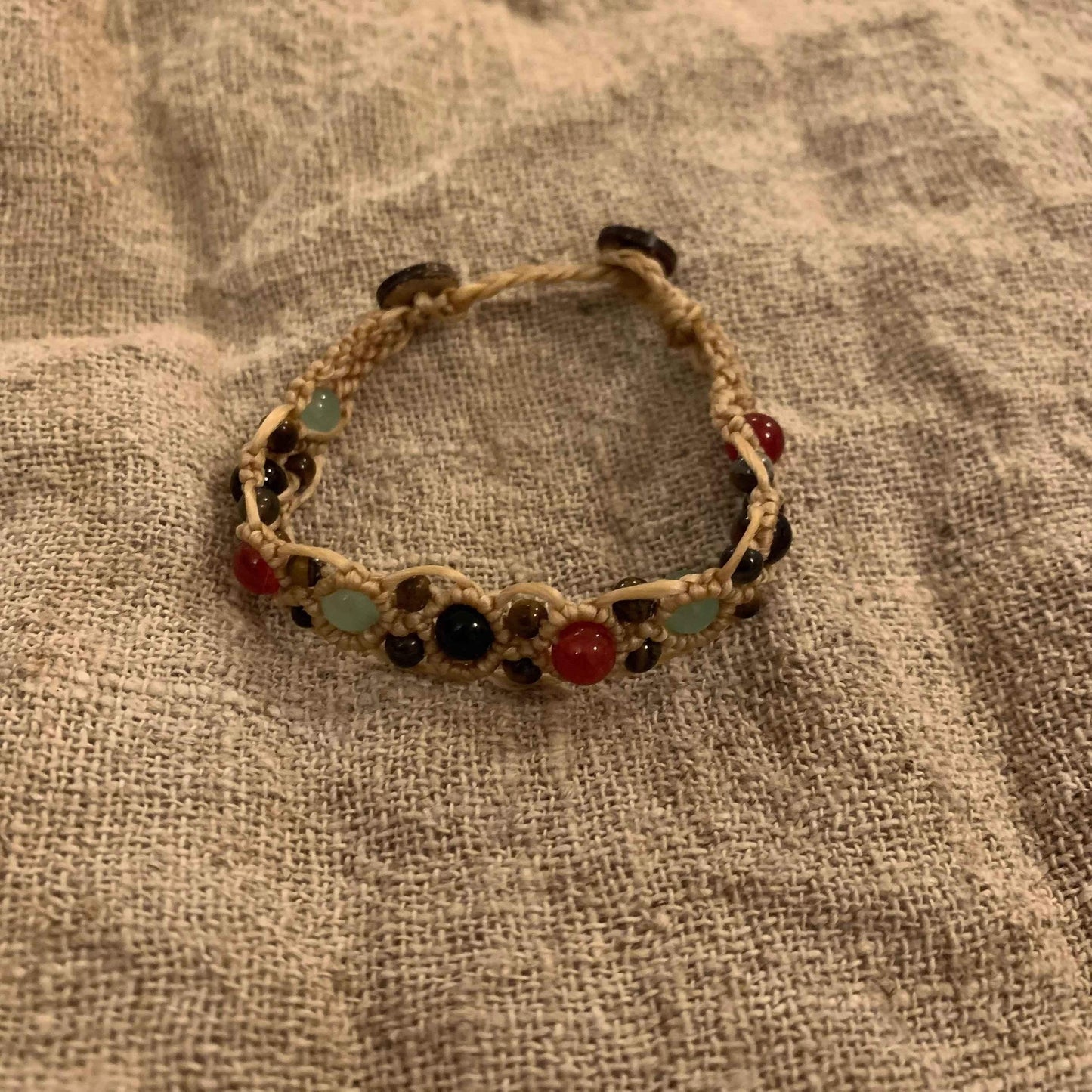 Handcrafted macrame bracelet with red, green, and black beads on natural cord, ethical jewelry