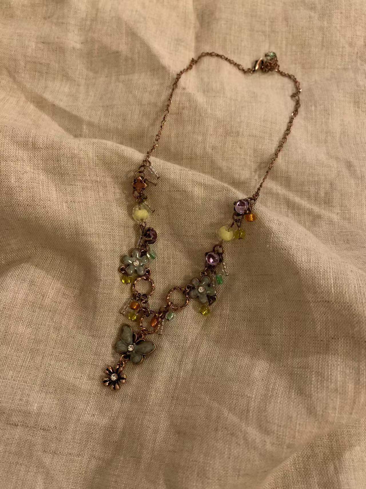 Floral charm necklace with colorful beads and gemstones on a textured fabric background
