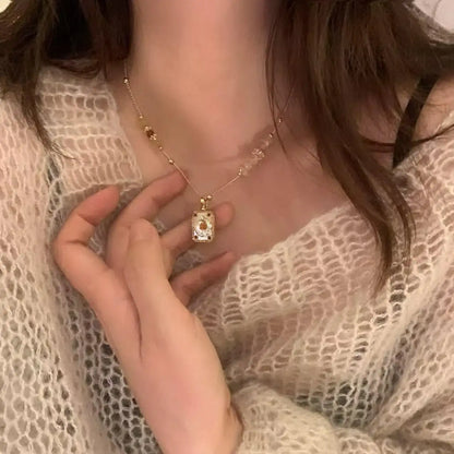 Minimalist gold necklace with rectangular pendant and delicate chain, worn with lace top