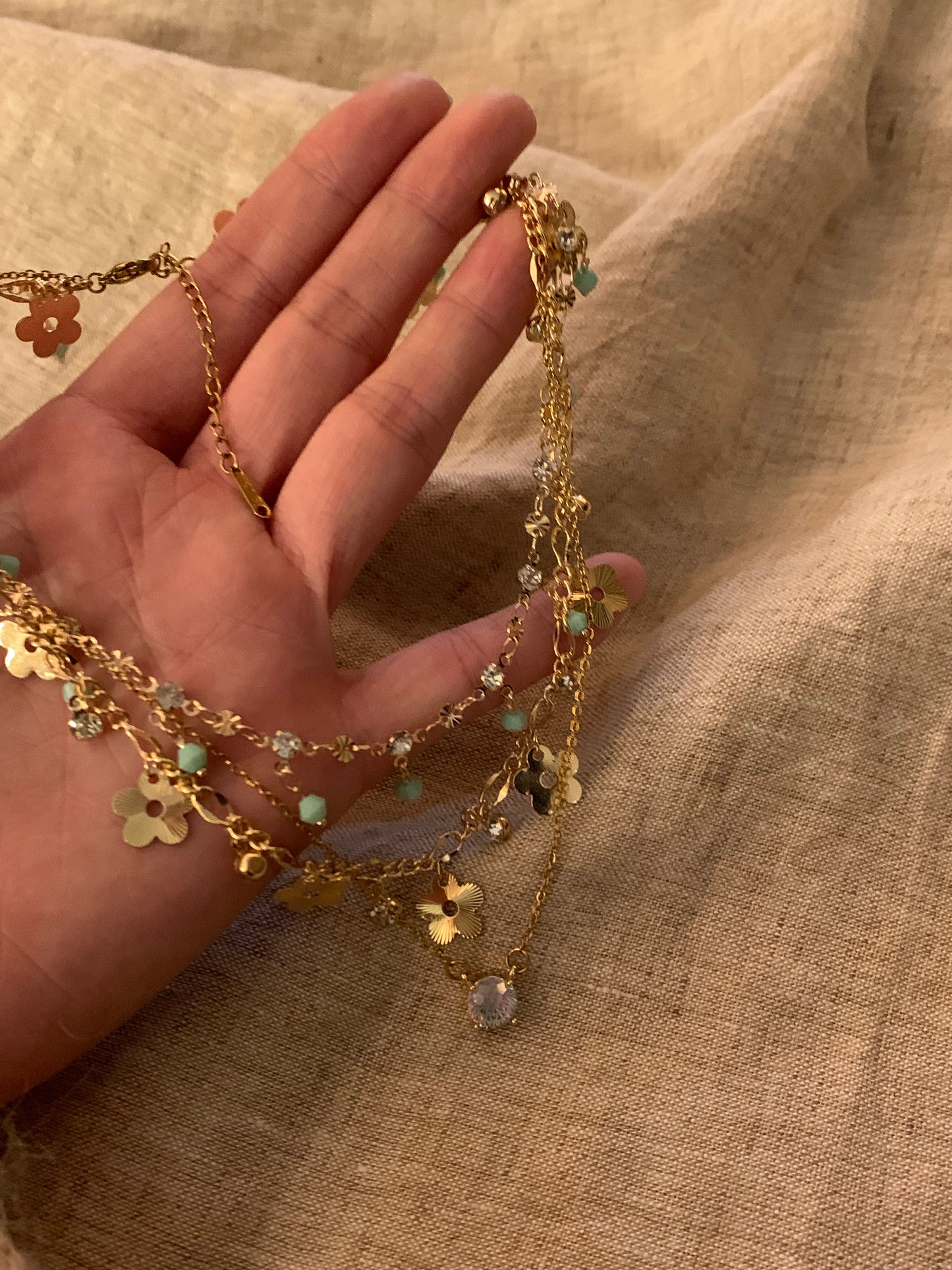 Gold necklace with floral and gemstone details held by a hand against a beige fabric background