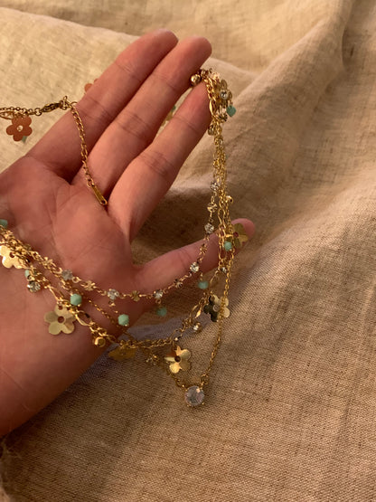 Gold necklace with floral and gemstone details held by a hand against a beige fabric background