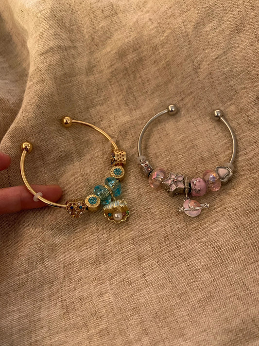 Two charm bangles with colorful beads and heart charms, gold and silver tone, on fabric background