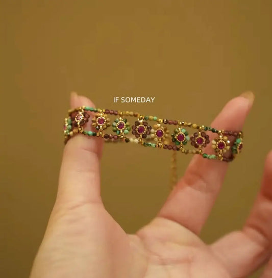 Hand holding a beaded bracelet with floral designs and colorful gemstones, showcasing intricate craftsmanship.
