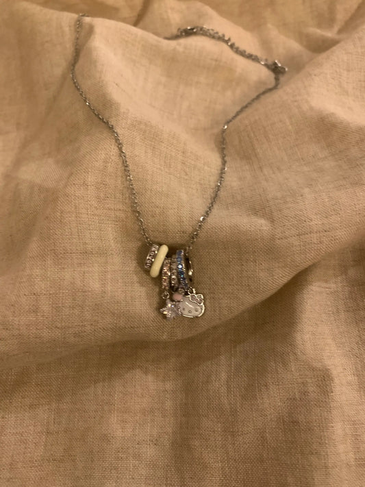 Silver chain necklace with Hello Kitty charm, beads, and crystals on beige fabric