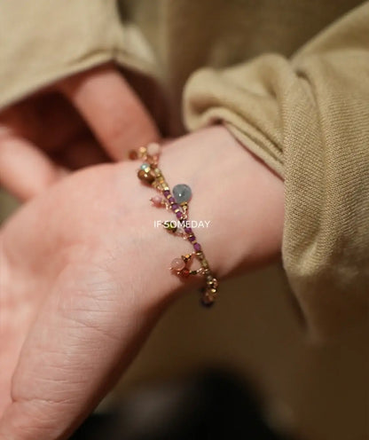 Delicate beaded bracelet with colorful gemstones and gold chain, worn on wrist with soft beige sleeve