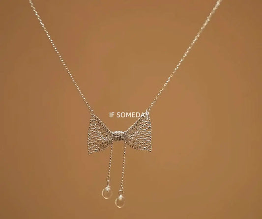Delicate silver bow necklace with pearl drop charms, minimalist jewelry design
